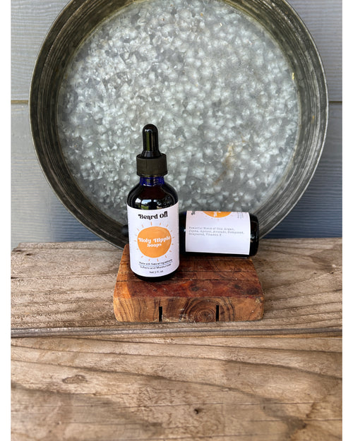 2 small dark glass dropper bottles labeled 'Beard Oil' on a rustic wooden soap saver, with a large galvanized metal tray behind them on a wood plank surface.